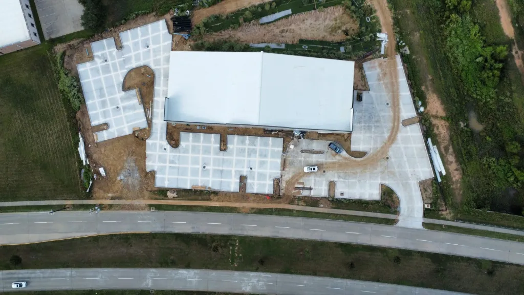 Aerial view of an active commercial construction site mid-build with multiple trades sequenced across phases.