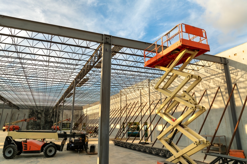 Construction Site with a Tall Steel Framework and Yellow Scissor Lift Raised Near a Ceiling Grid of Beams