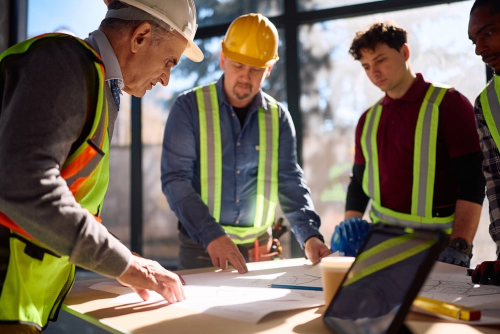 Construction team in high-visibility vests and hard hats examining blueprints on a table.