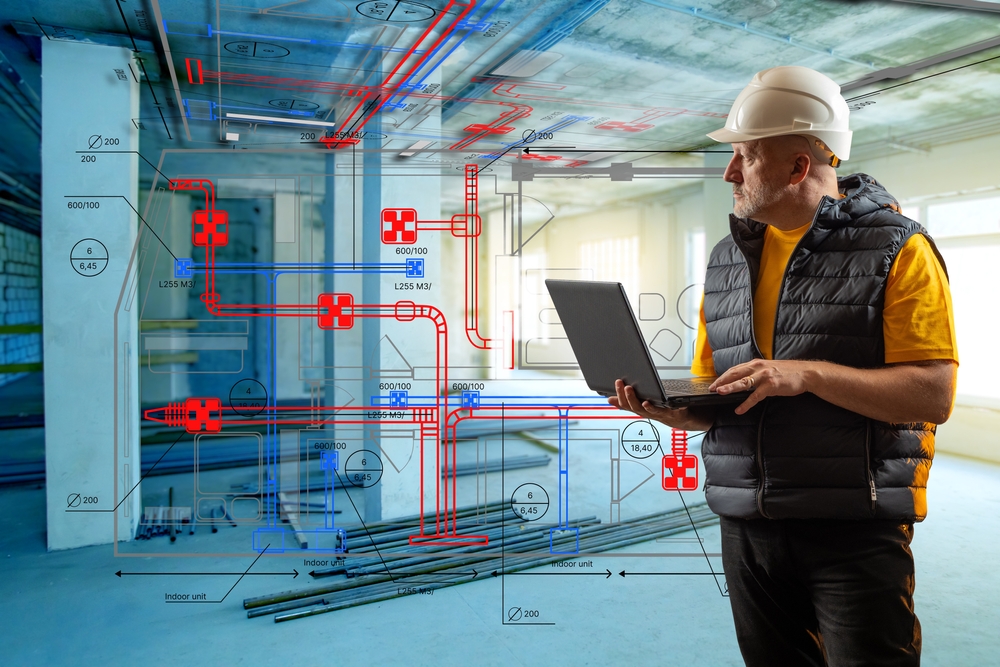 Construction worker with hard hat and vest using a tablet, overlaid with red and blue piping schematics in a building under construction.